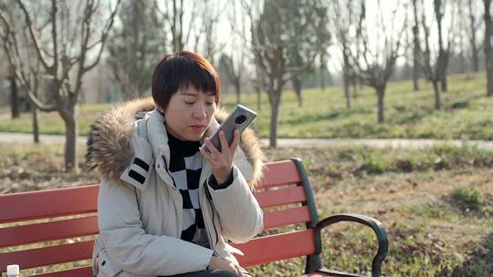 坐在公园长椅上使用手机的东方女性