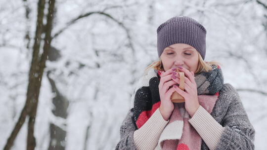 雪天女人穿着毛衣和鲜艳的围巾在公园里喝热茶视频素材模板下载