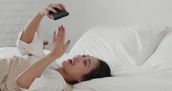 美女睡在床上看手机视频聊天