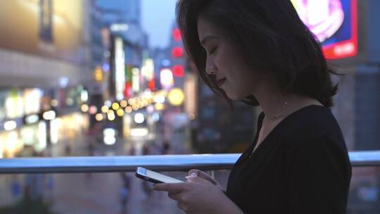 夏日城市女青年走在夜晚街头看手机