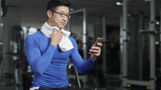 年轻人在健身房健身锻炼休息期间玩手机