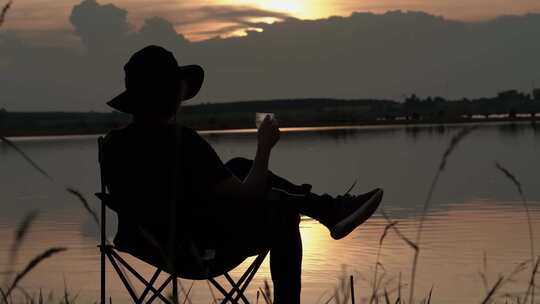 坐在河边折叠椅上看日出的年轻人