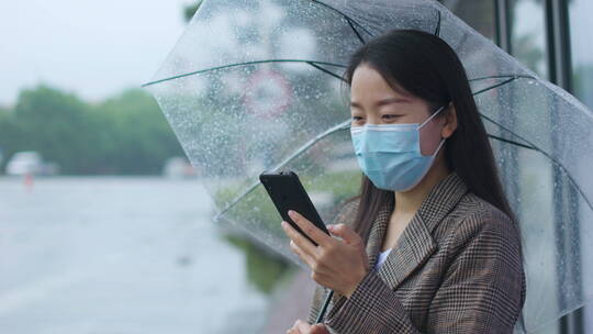 中国女性打伞步行踏春打电话等公交玩手机