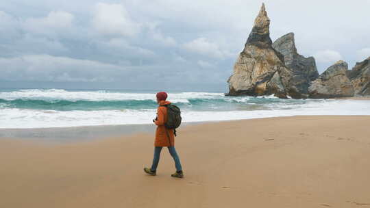 背着大背包的快乐男人沿着空旷的海洋海滩散步