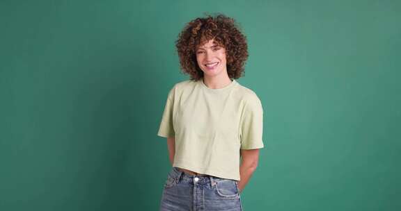 微笑着站在绿色背景上的年轻卷发女人