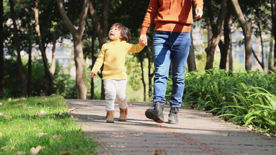 妈妈牵着小女儿的手走在阳光公园小路上