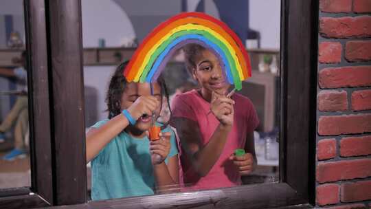 快乐的女孩在窗户上画明亮的彩虹