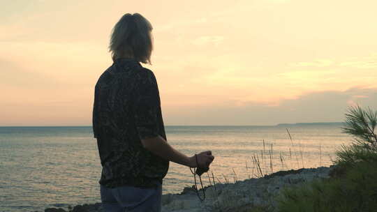 年轻的金发女子用模拟相机拍摄日落大海。