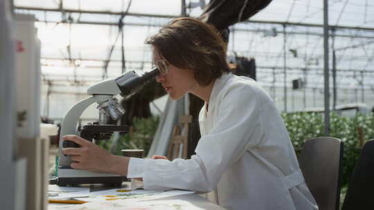 女植物学家在温室用显微镜进行研究