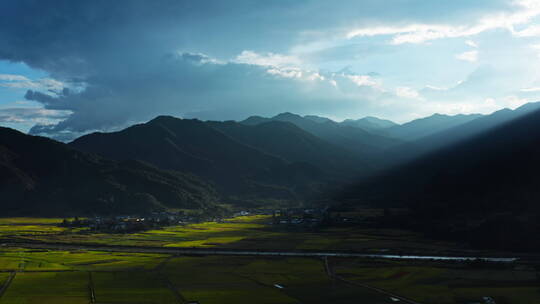 夕阳透过云层打在山脚的金黄稻田上