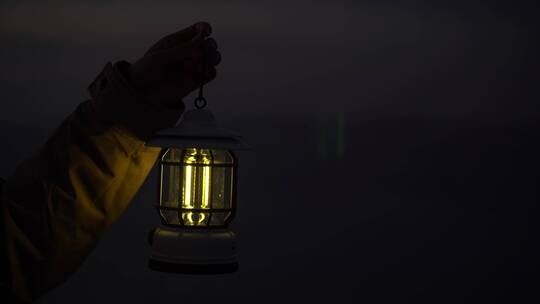 夜晚一个人手里提着一盏灯照亮黑夜站在海边
