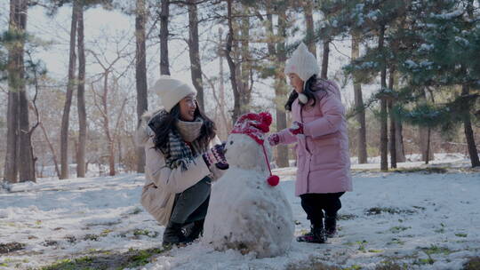 年轻妈妈和女儿在雪地里堆雪人