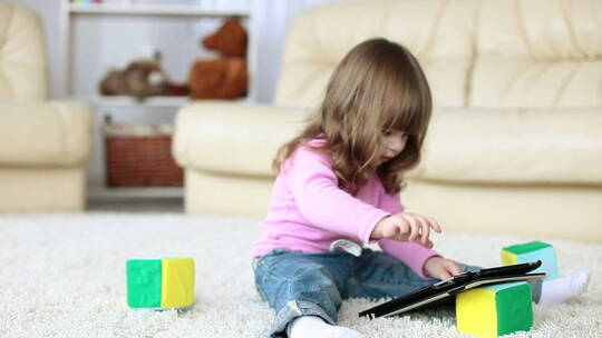 小女孩坐在地毯上玩平板电脑视频素材模板下载