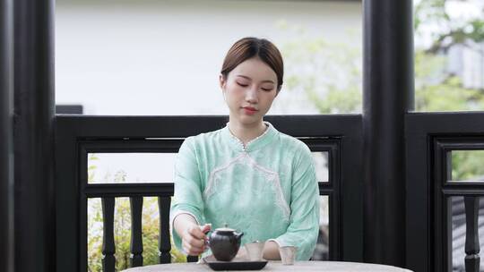 年轻旗袍女子坐在连廊里喝茶休息