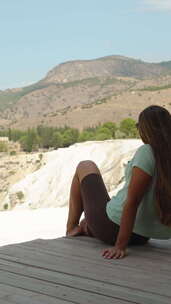 垂直视频。一名年轻女子坐在白山顶上的木桥