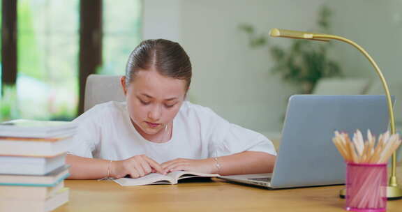 桌子上专注的少女用手指读一本书笔记本电脑旁边的跟踪线