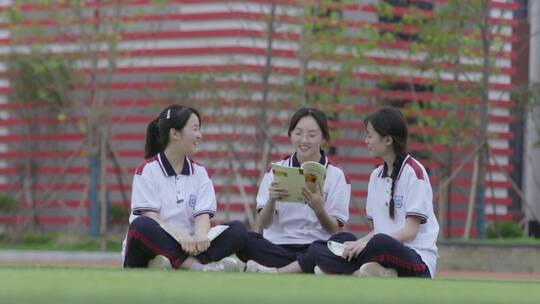 三个女学生坐在操场上看书聊天