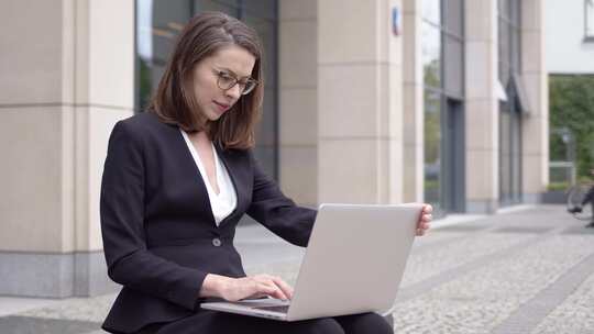 身着正式服装的妇女在办公楼外使用笔记本电脑
