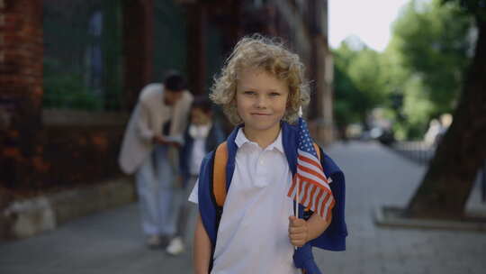 拿着美国国旗站在学校附近的小男孩肖像