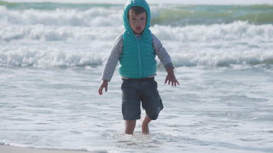 穿着背心的蹒跚学步的男孩正在海边玩沙子。