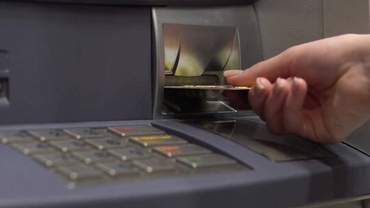 一名年轻女子将银行卡插入自动取款机。