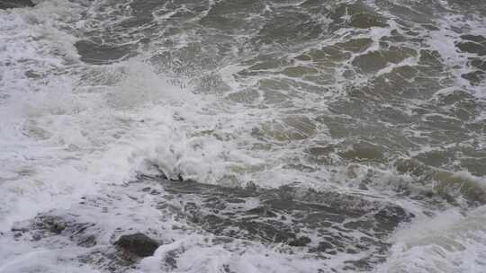 海浪拍打岩石浑浊海水冲刷礁石浪花阴天大海