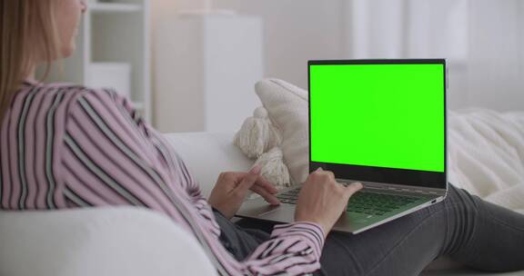 女人坐在沙发上看绿屏笔记本电脑