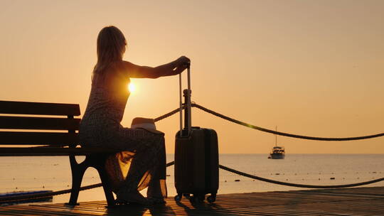 日落时分一个成年女人坐在长椅上手里拿着一个手提箱