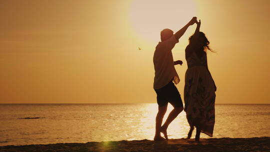 情侣在日落前的海边与夕阳伴舞