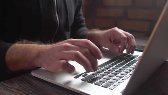 阁楼咖啡馆里，男人在笔记本电脑键盘上打字。特写男人双手在笔记本电脑键盘上写字。