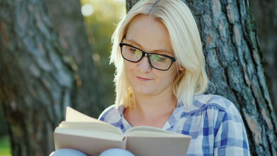 金发女子坐在树旁看书