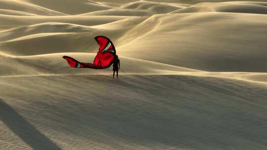 一个拿着红色风筝的人站在沙丘上，在刮风的日子里看着巴西的沙漠