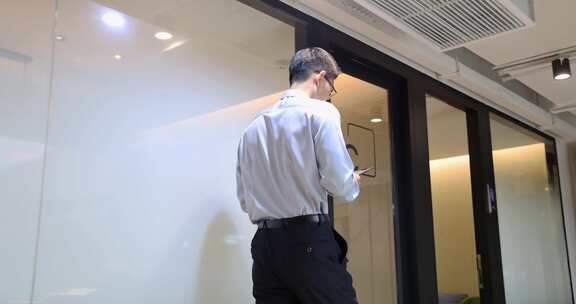 商务人士手拿平板电脑经过会议室前的走廊