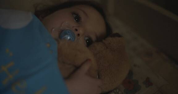 小女孩吸奶嘴抱小熊在床上睡觉
