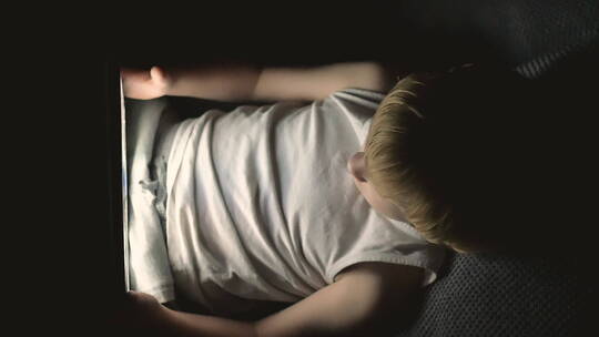 夜晚小男孩躺在沙发上看平板视频素材模板下载