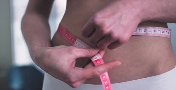 女人用卷尺测量自己的腰围