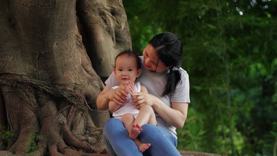 公园里大树下妈妈抱着小宝宝玩耍