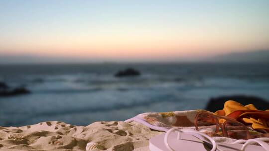夏日度假概念海滩毛巾带人字拖泳衣和太阳镜对抗日落天空视频素材模板下载