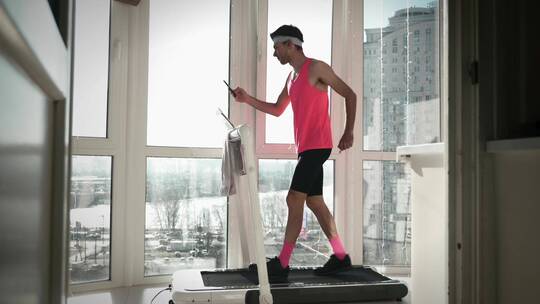 男人手拿手机在跑步机上锻炼视频素材模板下载