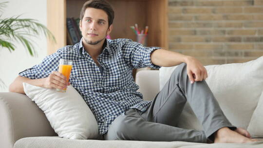 男人拿着一杯果汁半躺在沙发上