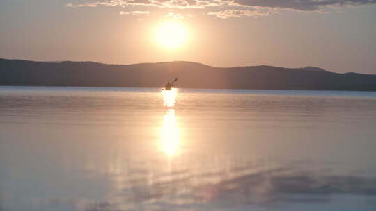 日落时男人在湖上划独木舟的远景