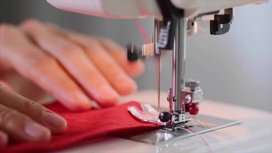 女裁缝的手在缝纫机上缝制红色衣服的直缝。