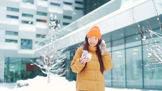 年轻美丽的亚洲女人在冬天下雪天听耳机里的