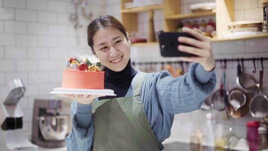 年轻女烘培师托着蛋糕微笑用手机自拍