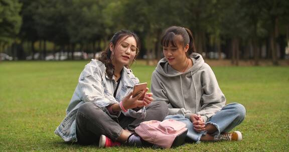 两位女大学生在校园草地上看手机自拍开心