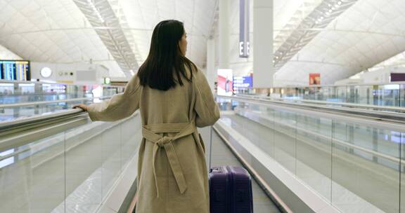 女人拉着手提箱在机场扶梯上