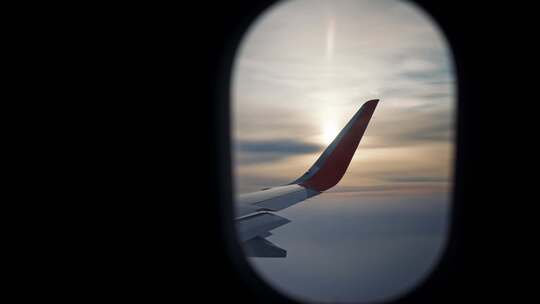 从飞机机翼上的窗户观看，在黎明或日落时在高空飞行时照射阳光