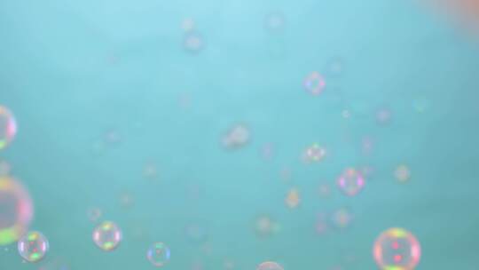 美丽的彩色肥皂泡被粉色灯光照亮，在蓝色背景下飞向室内