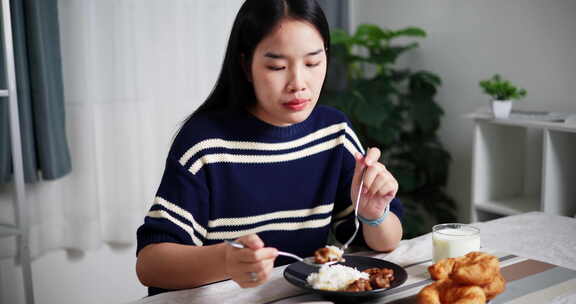 年轻的亚洲女人在家里的餐桌上享受美食。