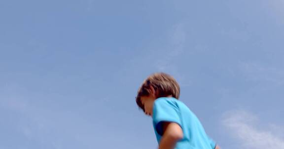 小男孩抱着足球在蓝天下跳跃